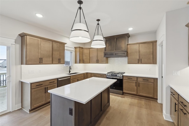 kitchen with sink, a center island, stainless steel appliances, decorative light fixtures, and light wood-type flooring