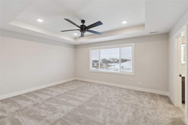 empty room with light carpet, a tray ceiling, and ceiling fan