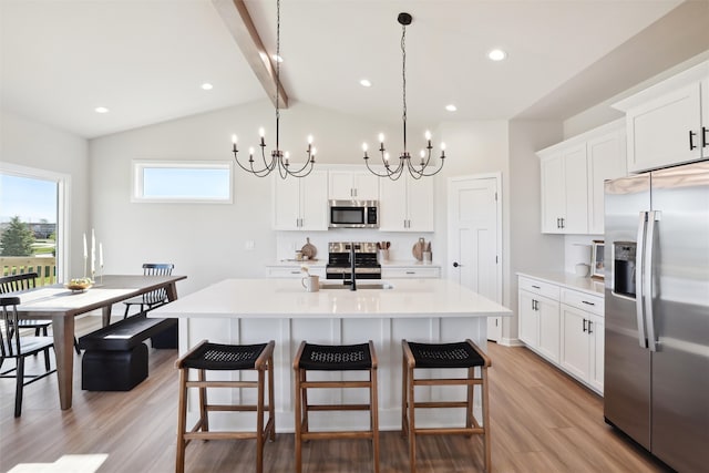 kitchen with lofted ceiling with beams, stainless steel appliances, pendant lighting, an island with sink, and light hardwood / wood-style floors