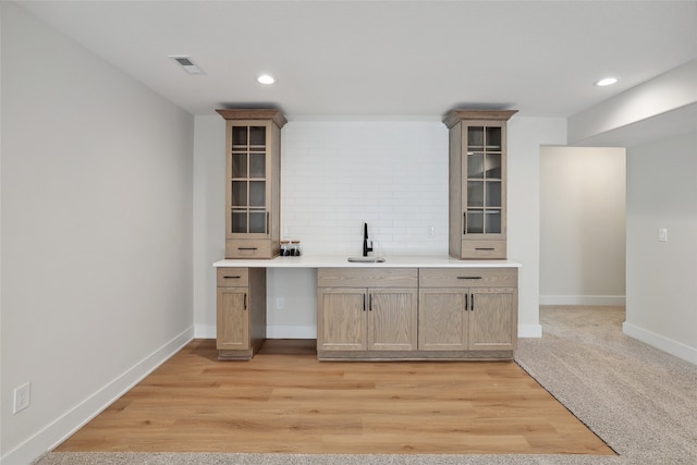 bar with light hardwood / wood-style floors, light brown cabinetry, and sink