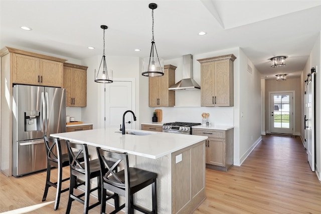 kitchen with a barn door, a kitchen island with sink, light hardwood / wood-style floors, wall chimney exhaust hood, and stainless steel appliances