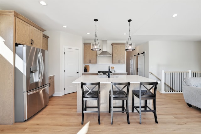 kitchen with wall chimney exhaust hood, a barn door, stainless steel refrigerator with ice dispenser, and an island with sink