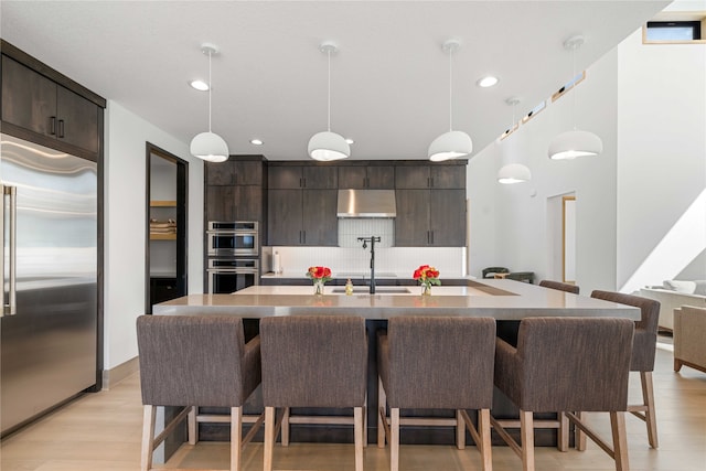 kitchen with stainless steel appliances, extractor fan, decorative light fixtures, and a center island with sink