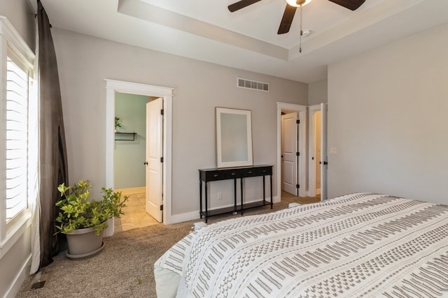 bedroom featuring a tray ceiling, light colored carpet, connected bathroom, and ceiling fan