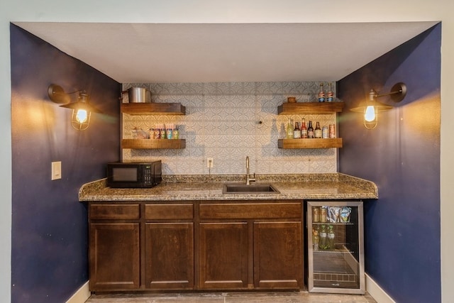 bar with wine cooler, dark brown cabinets, backsplash, dark stone countertops, and sink