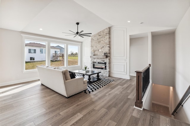 living room featuring vaulted ceiling, a stone fireplace, light wood-type flooring, and ceiling fan