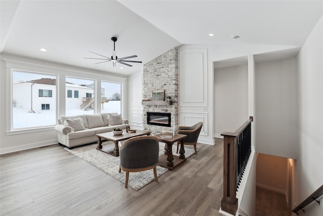 living room with ceiling fan, a fireplace, vaulted ceiling, and light hardwood / wood-style flooring