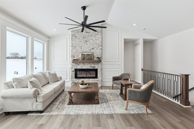 living room with ceiling fan, a stone fireplace, vaulted ceiling, and light hardwood / wood-style flooring