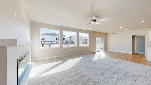 unfurnished living room with light carpet, a wealth of natural light, and ceiling fan