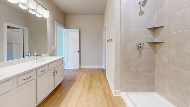 bathroom with hardwood / wood-style flooring, tiled shower, and vanity