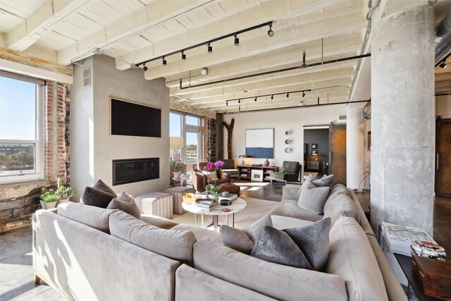 living room featuring beamed ceiling, concrete floors, track lighting, and brick wall