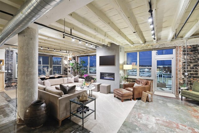 living area with beam ceiling, concrete flooring, a glass covered fireplace, and rail lighting