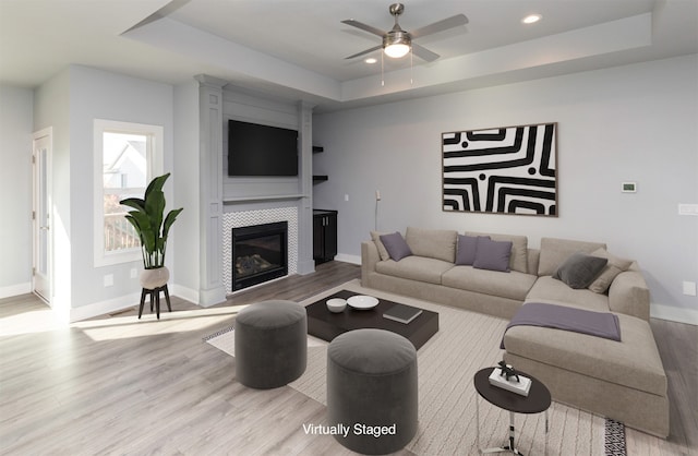 living room with light hardwood / wood-style flooring, a tray ceiling, and a fireplace