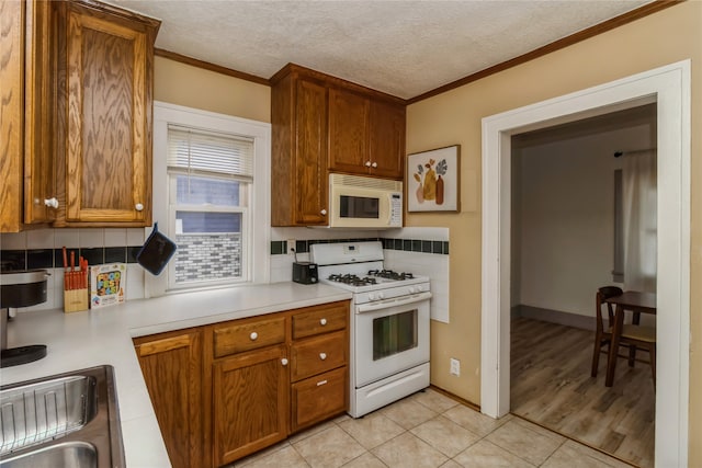 kitchen featuring light tile patterned floors, backsplash, a textured ceiling, crown molding, and white appliances