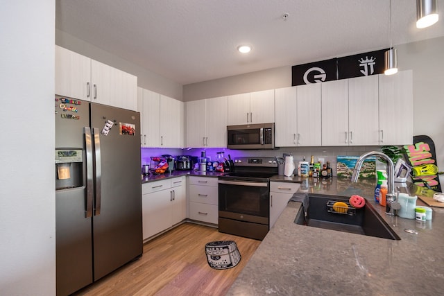 kitchen with appliances with stainless steel finishes, white cabinetry, light wood-type flooring, pendant lighting, and sink