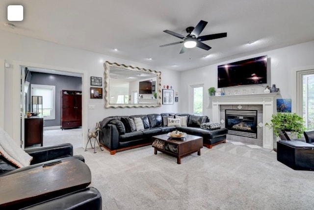 living room featuring a tiled fireplace, light colored carpet, a healthy amount of sunlight, and ceiling fan