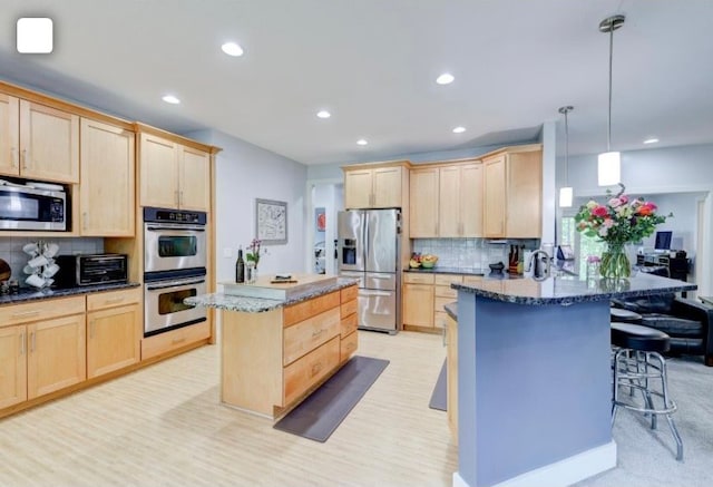 kitchen featuring tasteful backsplash, appliances with stainless steel finishes, a kitchen bar, decorative light fixtures, and a center island