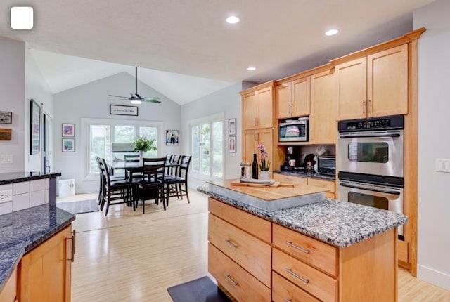 kitchen featuring dark stone counters, vaulted ceiling, light wood-type flooring, appliances with stainless steel finishes, and ceiling fan