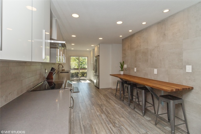 kitchen with a breakfast bar, stainless steel fridge, light wood-type flooring, tile walls, and white cabinetry