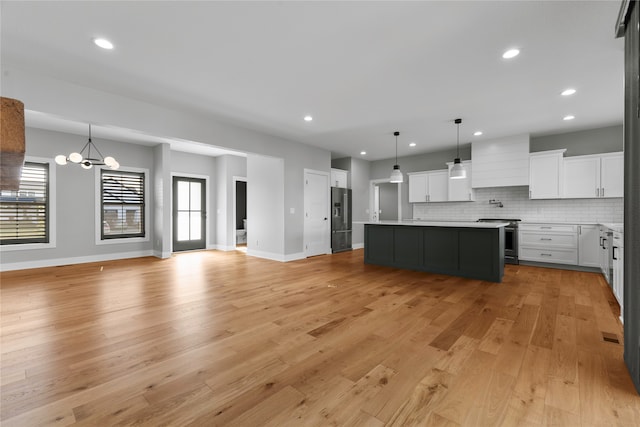 kitchen with a kitchen island, stainless steel appliances, decorative light fixtures, white cabinets, and light hardwood / wood-style floors