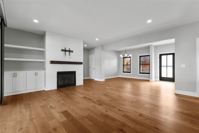 unfurnished living room featuring built in features, a notable chandelier, a fireplace, and light wood-type flooring