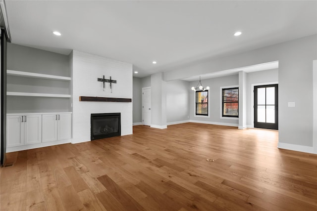 675 Daybreak Dr, Waukee, IA 50263 - unfurnished living room with light wood-style flooring, baseboards, recessed lighting, a fireplace, and a notable chandelier