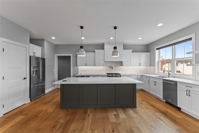 kitchen with a kitchen island, appliances with stainless steel finishes, light hardwood / wood-style flooring, pendant lighting, and sink