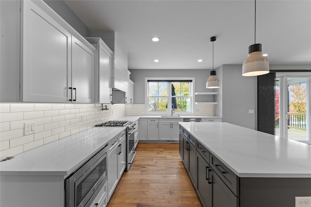 kitchen featuring light stone countertops, hanging light fixtures, stainless steel appliances, and light hardwood / wood-style floors