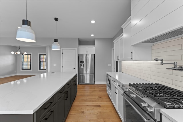 kitchen with tasteful backsplash, light wood-type flooring, white cabinetry, stainless steel appliances, and decorative light fixtures