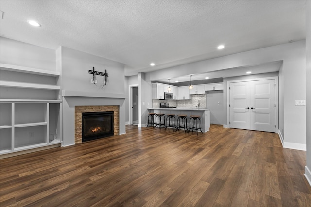 675 Daybreak Dr, Waukee, IA 50263 - unfurnished living room with a textured ceiling, dark wood-style floors, baseboards, recessed lighting, and a stone fireplace