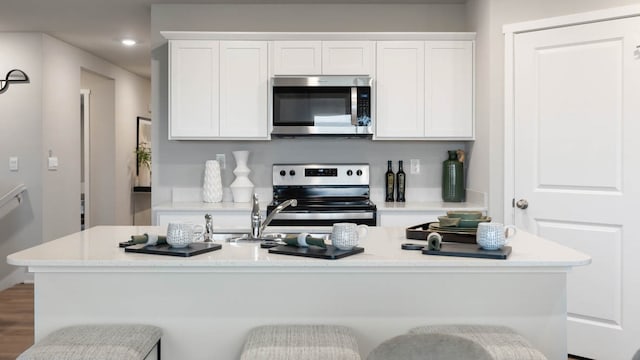 kitchen featuring appliances with stainless steel finishes, a breakfast bar, white cabinetry, and a center island with sink