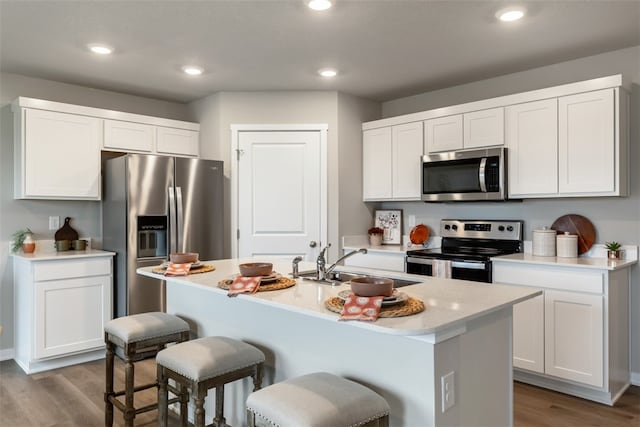 kitchen featuring appliances with stainless steel finishes, a kitchen island with sink, light wood-type flooring, white cabinets, and sink