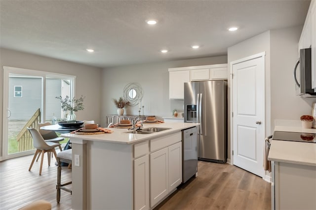 kitchen featuring light hardwood / wood-style floors, appliances with stainless steel finishes, a kitchen island with sink, white cabinets, and sink