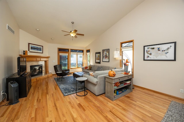 living area with high vaulted ceiling, a tile fireplace, a ceiling fan, visible vents, and light wood-style floors