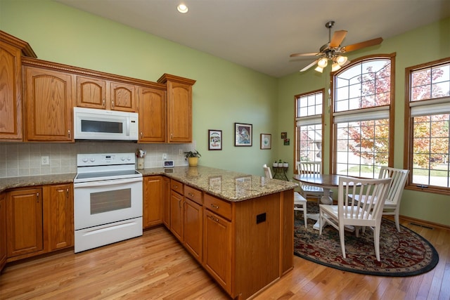 kitchen featuring light wood-type flooring, white appliances, a peninsula, and backsplash