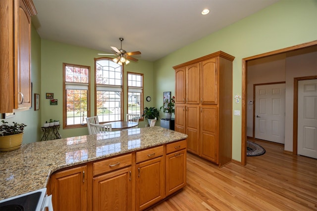 kitchen featuring light stone counters, light wood-style flooring, brown cabinetry, a ceiling fan, and a peninsula