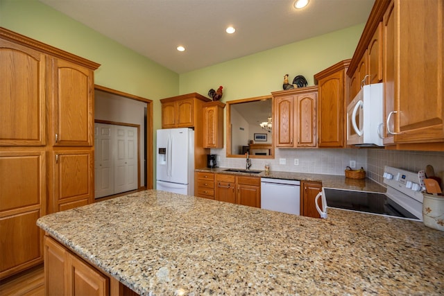 kitchen featuring white appliances, tasteful backsplash, a peninsula, light stone countertops, and a sink