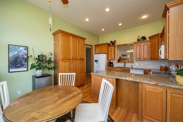 kitchen with a peninsula, white appliances, a sink, light wood-type flooring, and light stone countertops