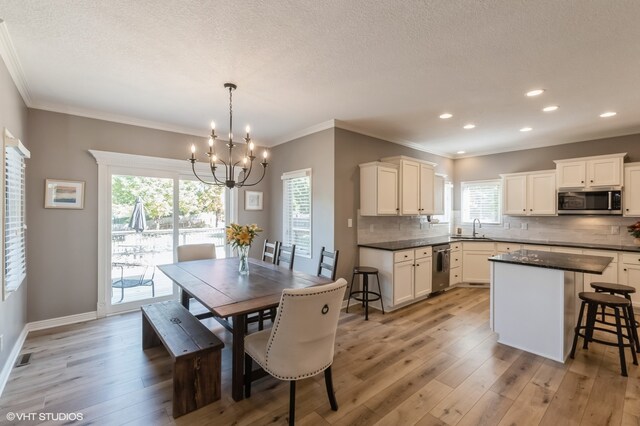 dining space featuring a notable chandelier, ornamental molding, sink, and light wood-type flooring