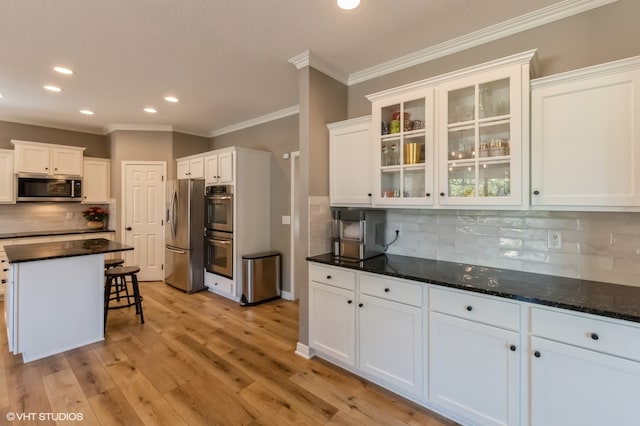 kitchen with appliances with stainless steel finishes, white cabinetry, light wood-type flooring, and a breakfast bar area