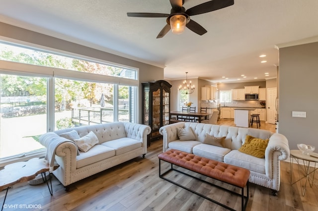 living room featuring ornamental molding, light hardwood / wood-style flooring, and ceiling fan with notable chandelier