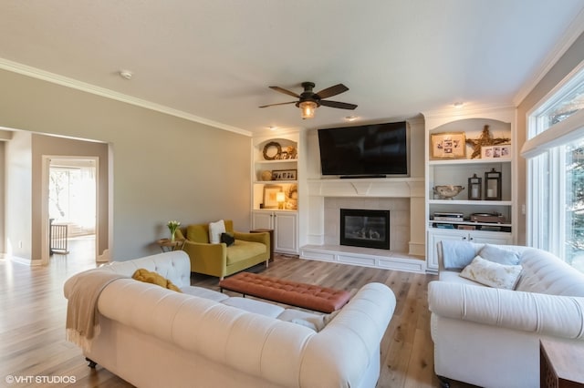 living room featuring ceiling fan, ornamental molding, light wood-type flooring, and a fireplace