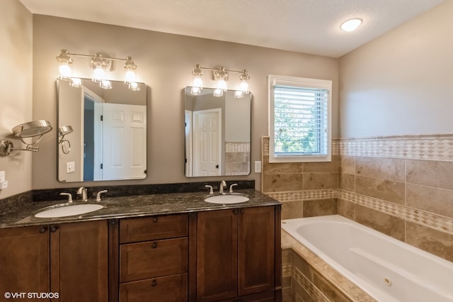 bathroom featuring vanity, a textured ceiling, and tiled tub