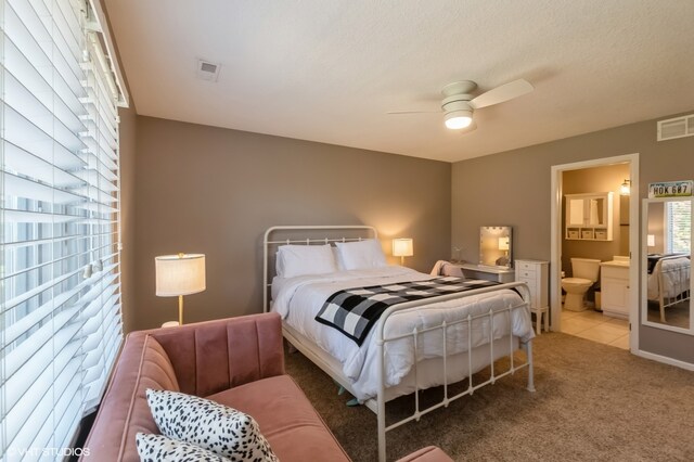 bedroom with a textured ceiling, light carpet, ensuite bathroom, and ceiling fan