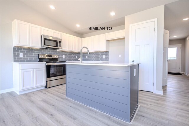 kitchen featuring sink, a kitchen island with sink, white cabinetry, stainless steel appliances, and vaulted ceiling