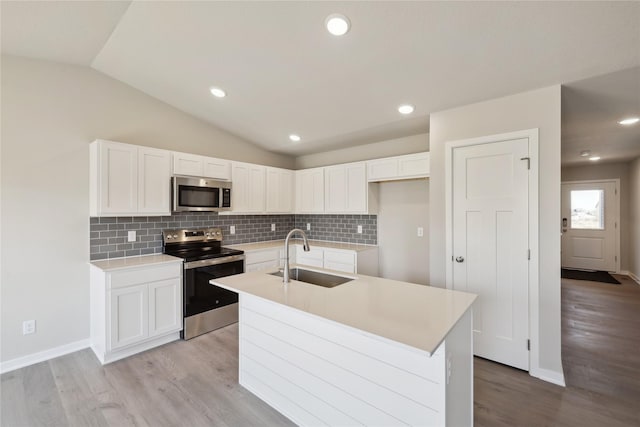 kitchen featuring tasteful backsplash, appliances with stainless steel finishes, white cabinets, vaulted ceiling, and a sink