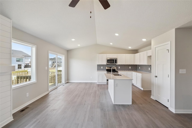 kitchen with stainless steel appliances, visible vents, vaulted ceiling, backsplash, and an island with sink