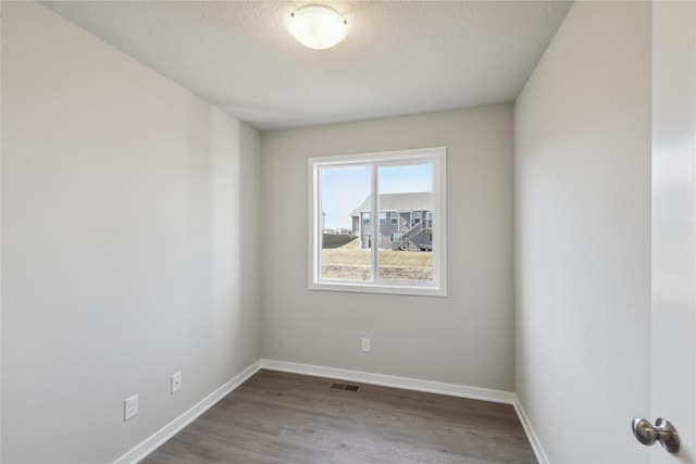 spare room featuring visible vents, a textured ceiling, baseboards, and wood finished floors