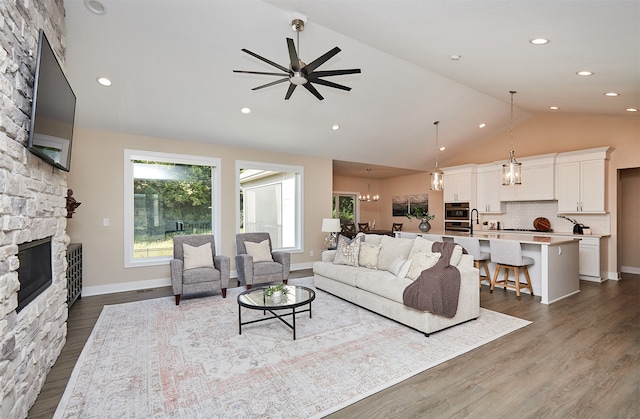 living room with high vaulted ceiling, a stone fireplace, dark hardwood / wood-style flooring, and ceiling fan with notable chandelier