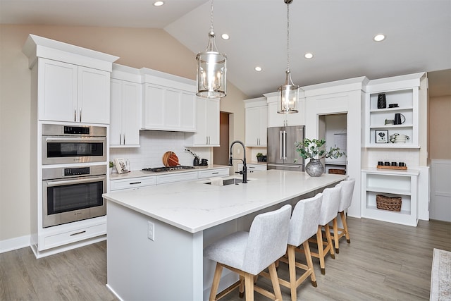 kitchen featuring lofted ceiling, a kitchen island with sink, stainless steel appliances, sink, and white cabinetry